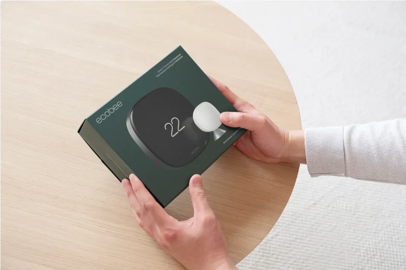 Hands holding the ecobee Smart Thermostat Premium retail box with SmartSensor included